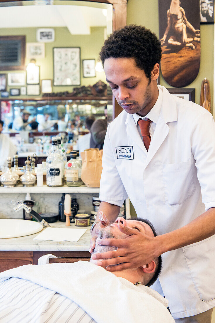 Professioneller Barbier und Haarschneider rasiert seinen Kunden im Schorem Barber Shop am Nieuwe Binnenweg, Rotterdam, Niederlande.