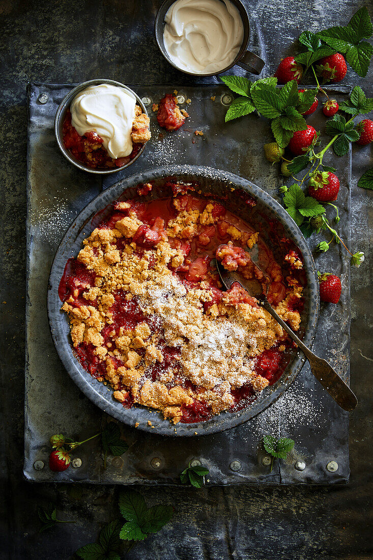 Homemade strawberry crumble served with whipped cream on a grey metal plate