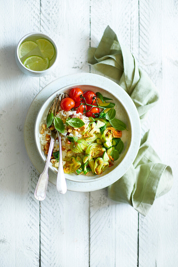 Fried courgette flowers, fried cherry tomatoes, basil and chopped hazelnuts, served in a white bowl on risotto rice, on a white wooden base