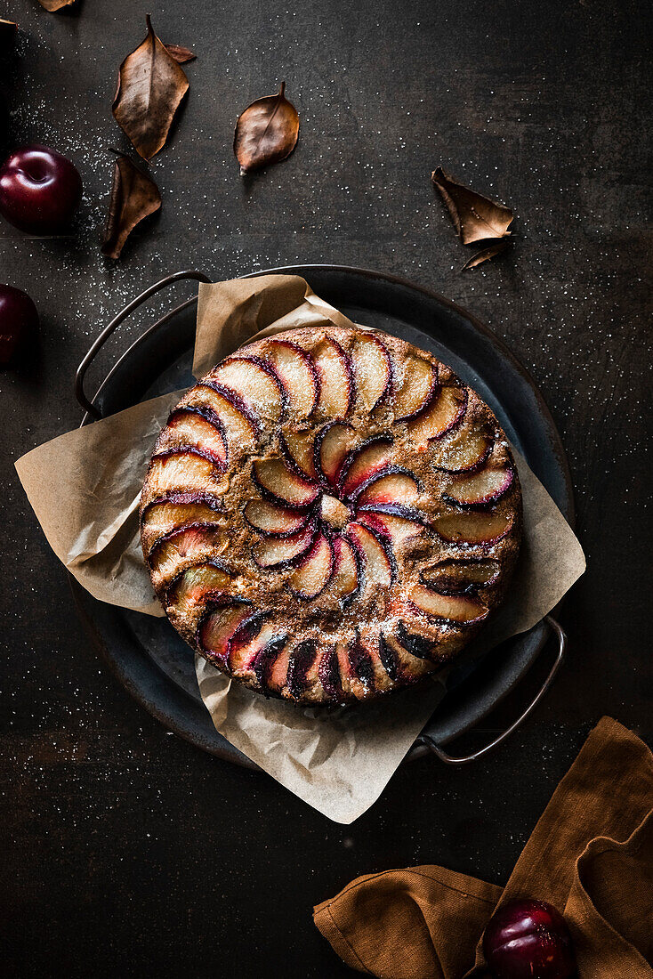 A rustic plum cake surrounded with autumn leaves and fresh fruit