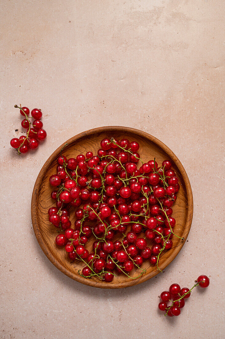 Rote Johannisbeeren auf einem Holzteller vor einem beigen Hintergrund