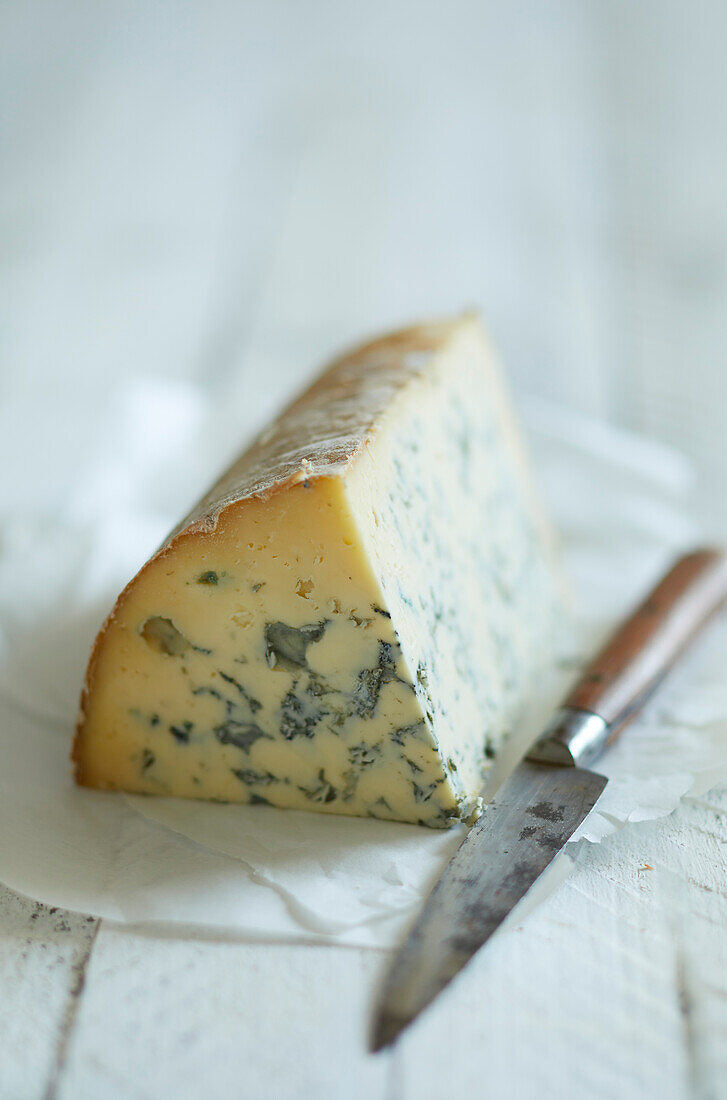 Ein schönes Stück Blauschimmelkäse auf einem weißen Papier mit einem Messer serviert