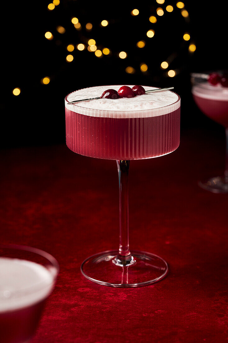 Mulled Wine Sour with Cranberries on Red Surface with fairy lights and glasses