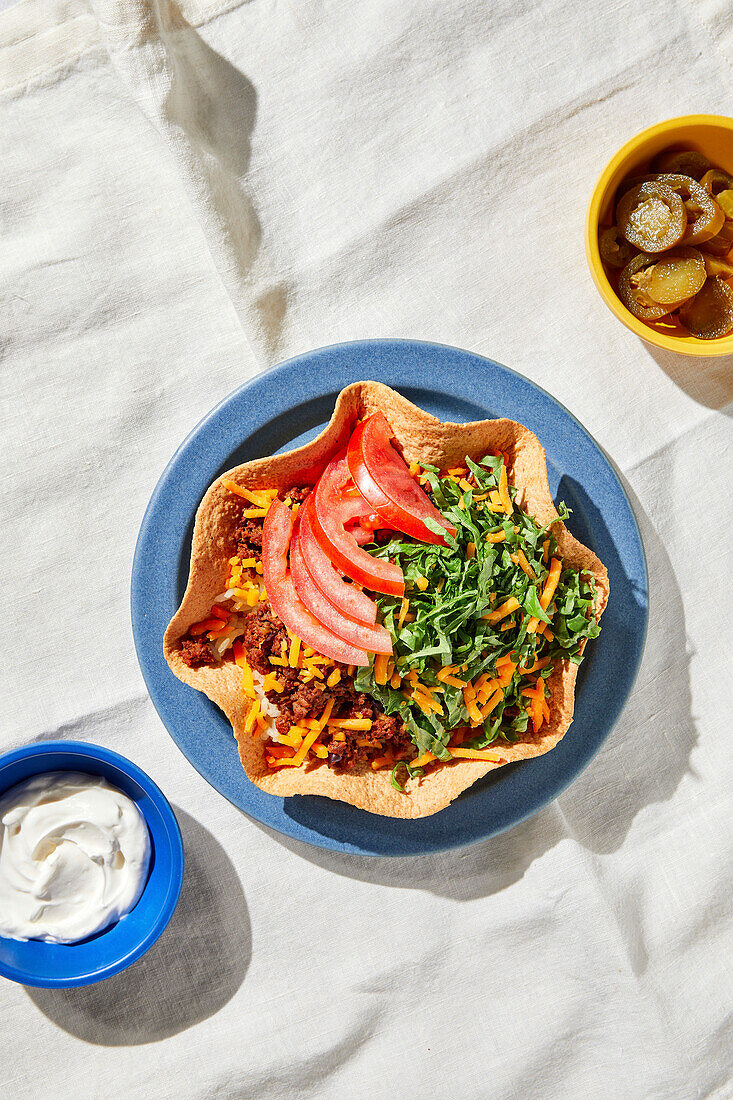 Beef taco bowl on a blue plate and white tablecloth with harsh light