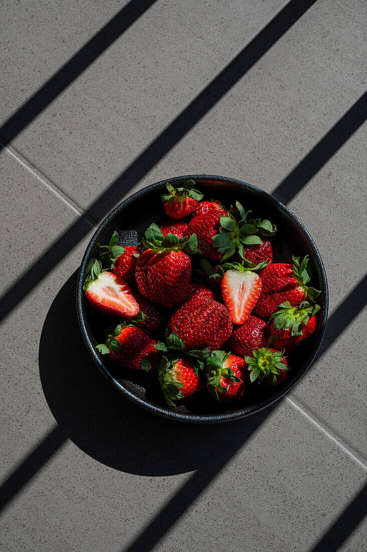 A bowl of strawberries in the blazing summer sun with strong shadows