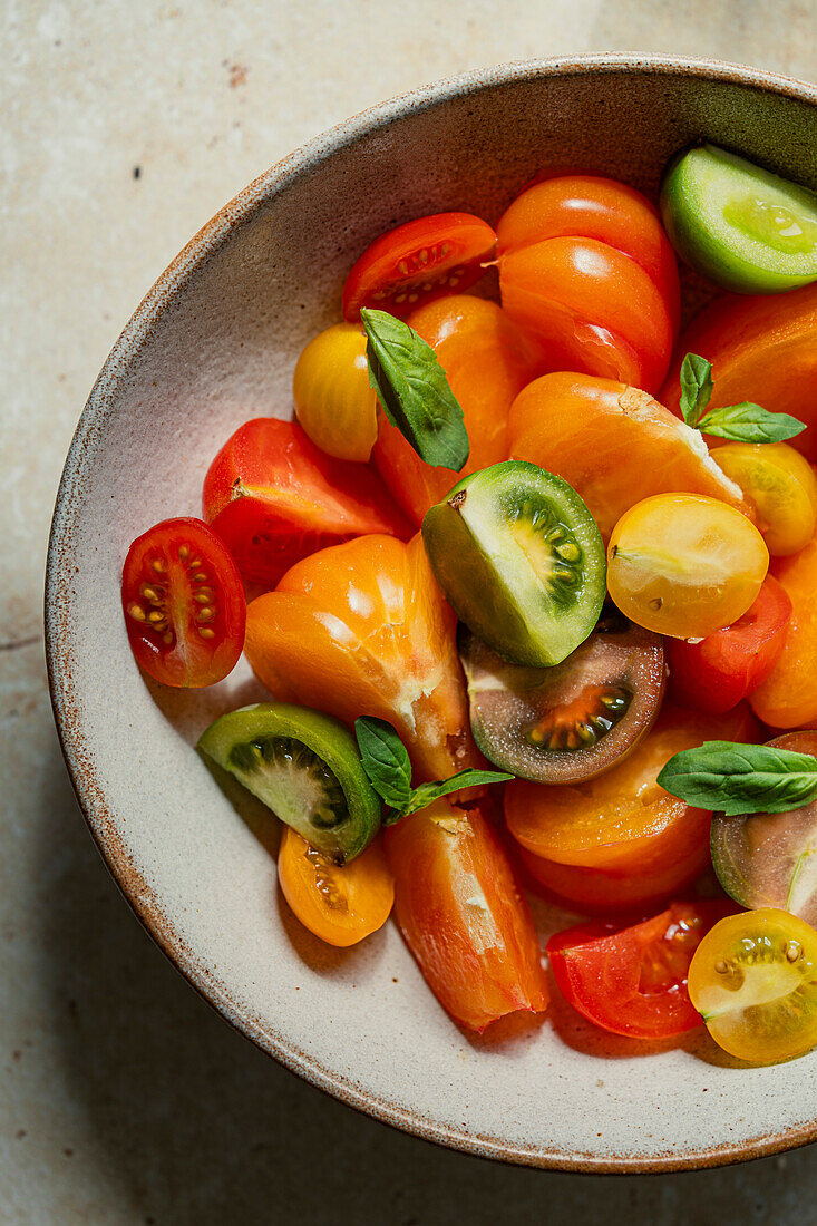 Nahaufnahme einer Schale mit bunten, frischen Tomaten und Basilikumblättern