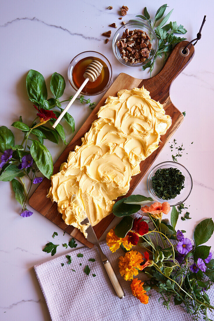 Zubereitung eines Butterbretts mit Kräutern, Pekannüssen und essbaren Blumen.