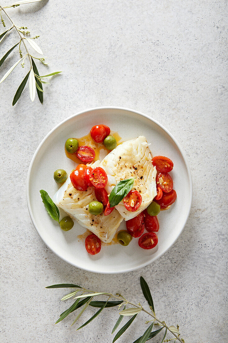 Fried cod with tomatoes and olives on a neutral background with olive branches