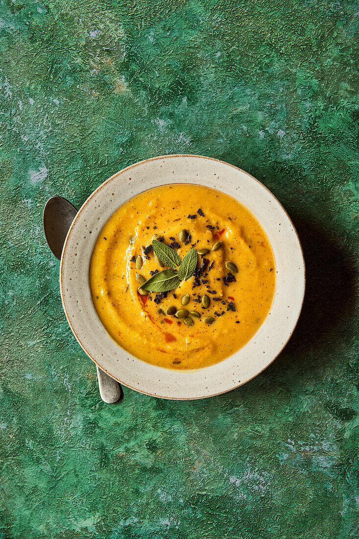 Kürbissuppe auf grüner Unterlage mit Salbei und Kürbiskernen