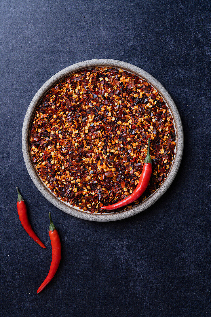 Chilli flakes on a plate of raw chillies on a blue background