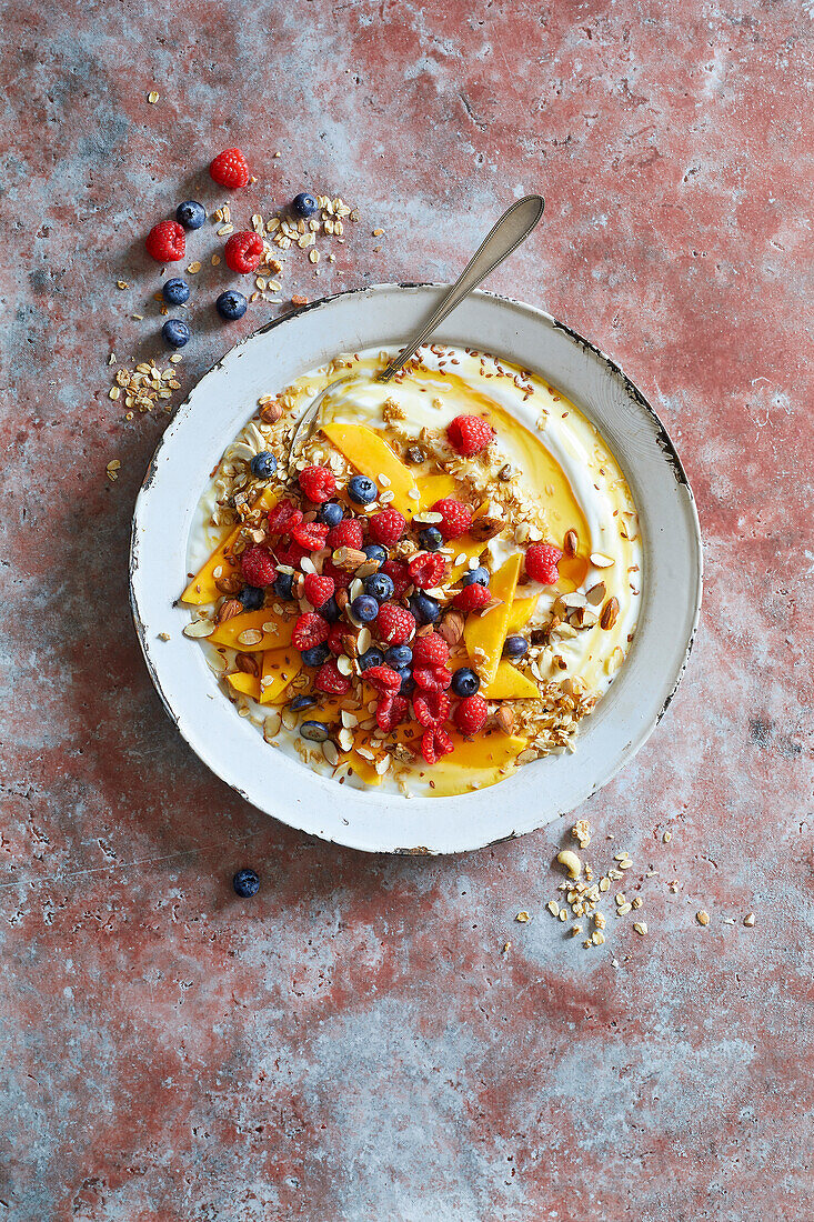 Muesli with yoghurt, fresh fruit and honey on a white plate