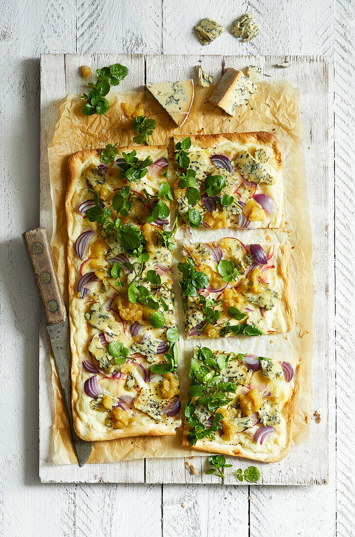 Homemade tarte flambée with blue cheese, pear chutney, red onions and watercress on a white wooden background