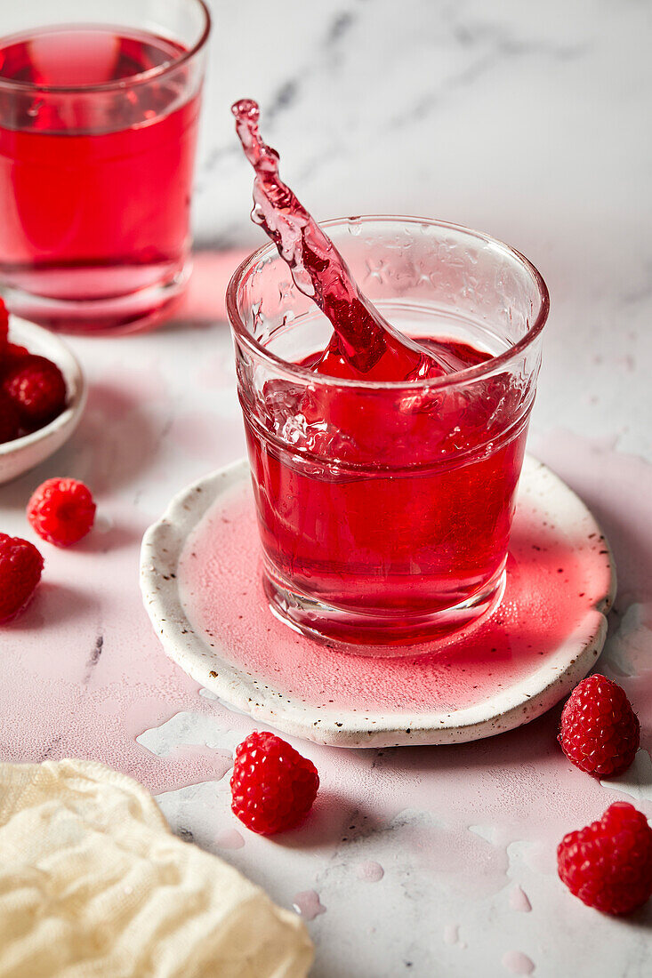 Splash photography of a glass of raspberry hibiscus ginger beer against a light marble background.