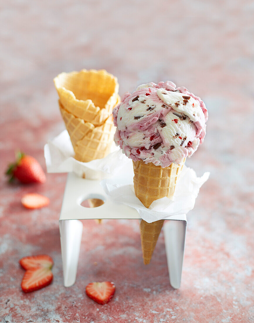 Erdbeereis in einer mit Erdbeeren verzierten Eistüte auf rotem Hintergrund