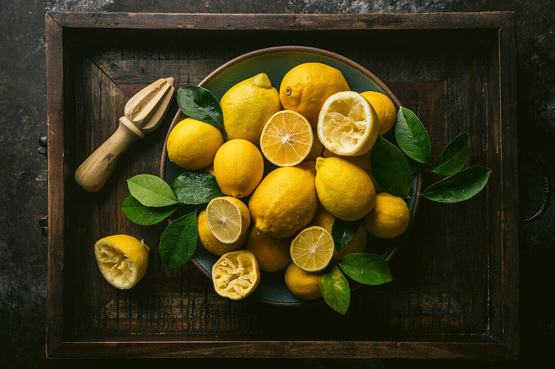 Variety of Lisbon and Meyer Lemons, some juiced, with fresh leaves, arrangred in blue ceramic bowl with wood juicer. Set in rustic wood box.