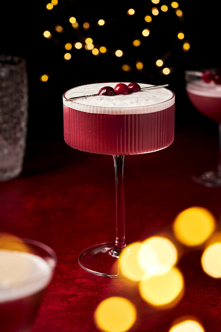 Mulled wine sour with cranberries on a red surface with fairy lights and glasses