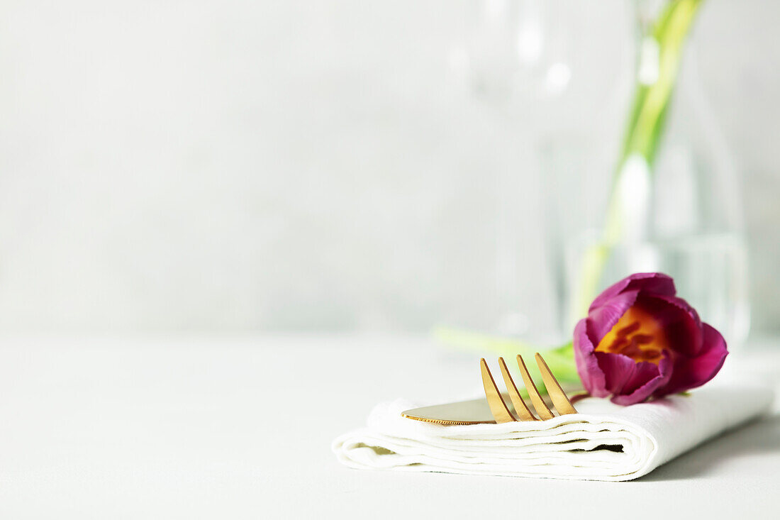 Goldenes Besteck und schöne Blume auf hellgrauem Tisch mit Platz für Text. Festlich gedeckter Tisch