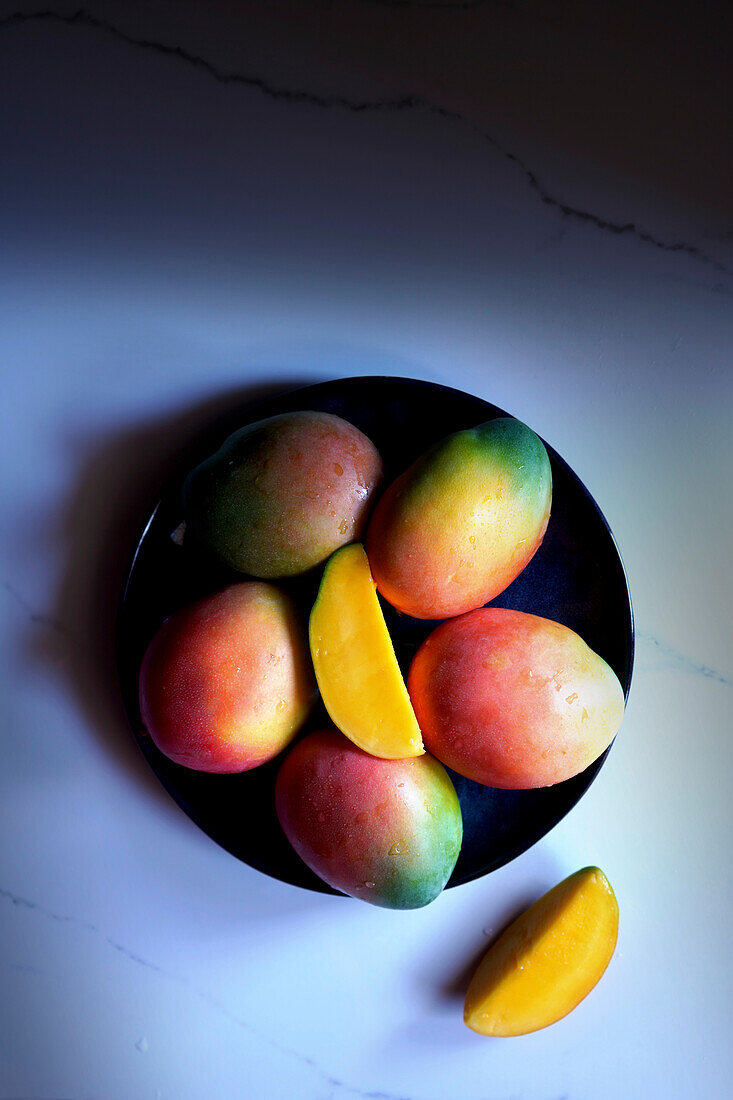 Teller mit bunten tropischen Sommerfrüchten wie Mangos. Flatlay von oben nach unten mit negativem Raum.