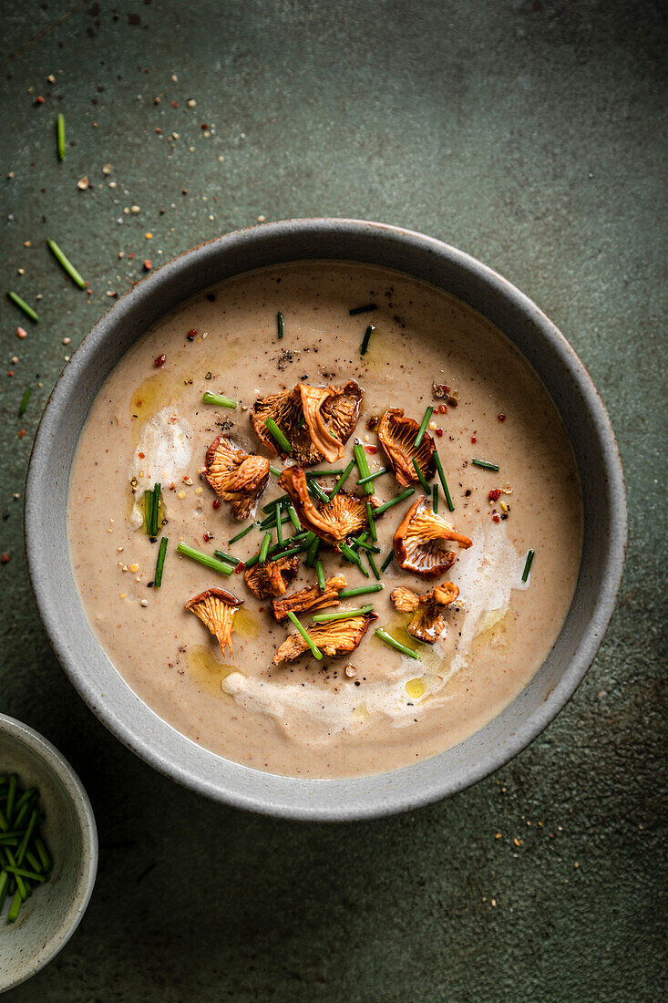 Mushroom soup topped with wild mushrooms on a green surface.