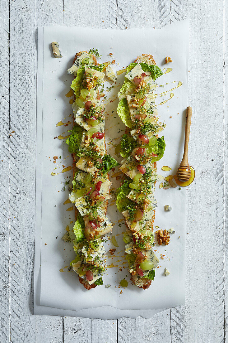 Two baguettes topped with blue cheese, grapes, salad, walnuts, cress and honey