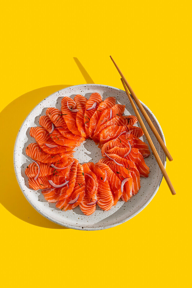 Salmon crudo on a white speckled plate in front of a yellow background