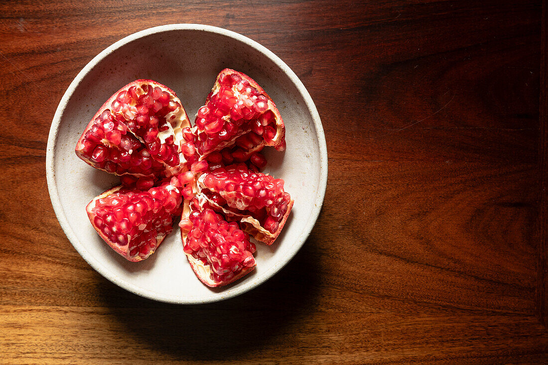 Pomegranate in a ceramic bowl on a wooden table.