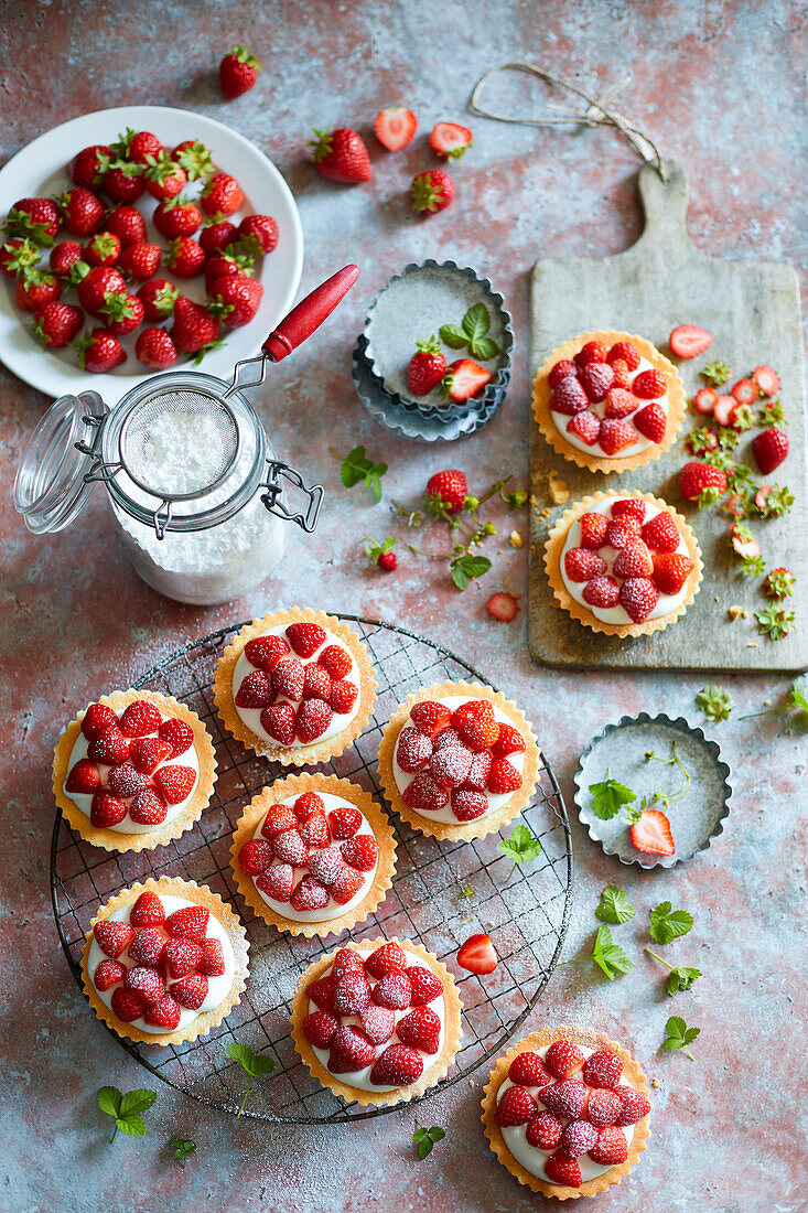 Tartlets filled with cream and strawberries on a wire rack, dusted with confectioners' sugar