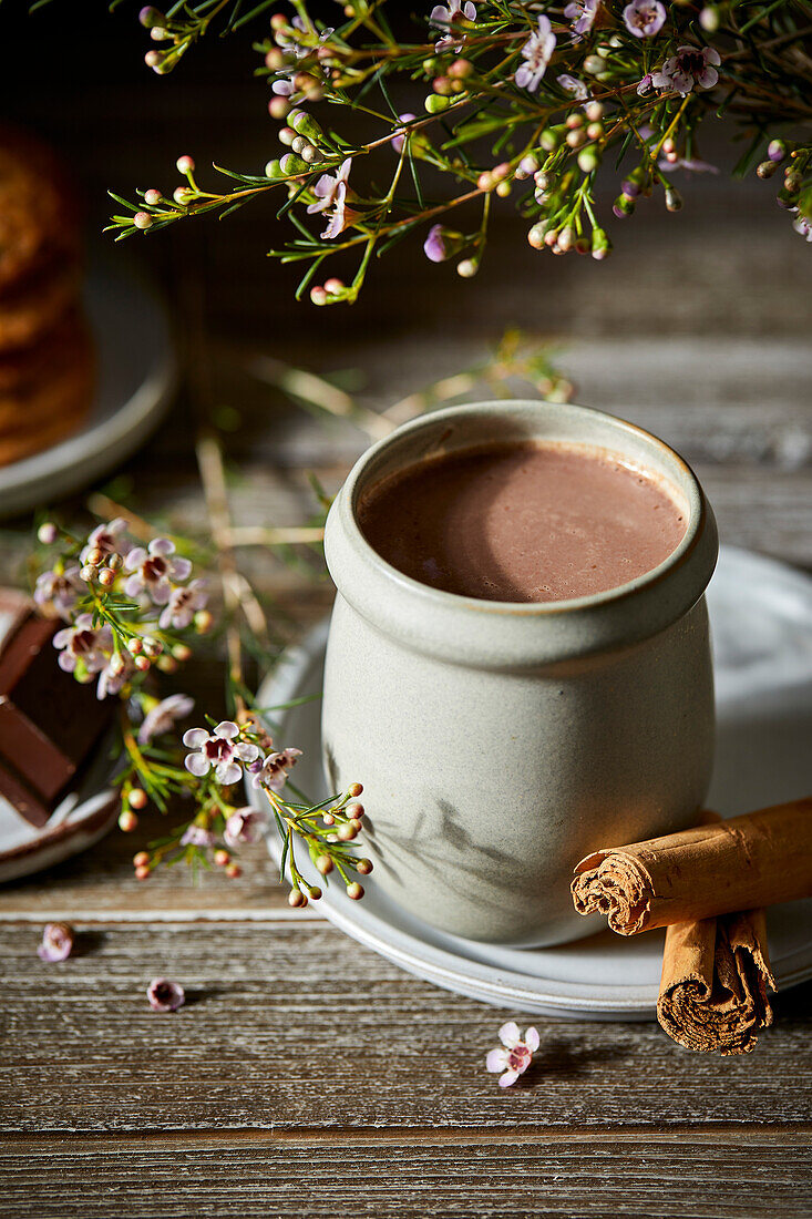 Mexikanische heiße Schokolade auf einem dunklen Holzhintergrund mit Blumen, Keksen und Zimtstangen.