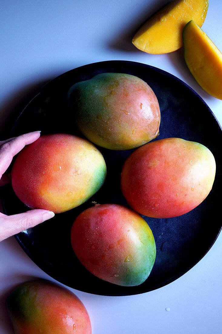 Plate of colorful mango tropical summer fruit. Top down flatlay with female hand.