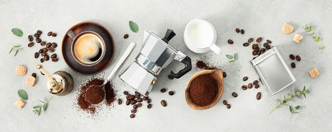 Flat lay with moka pot, espresso cup, ground coffee, milk, sugar and coffee beans on a grey concrete background. Header with ingredients for brewed coffee.