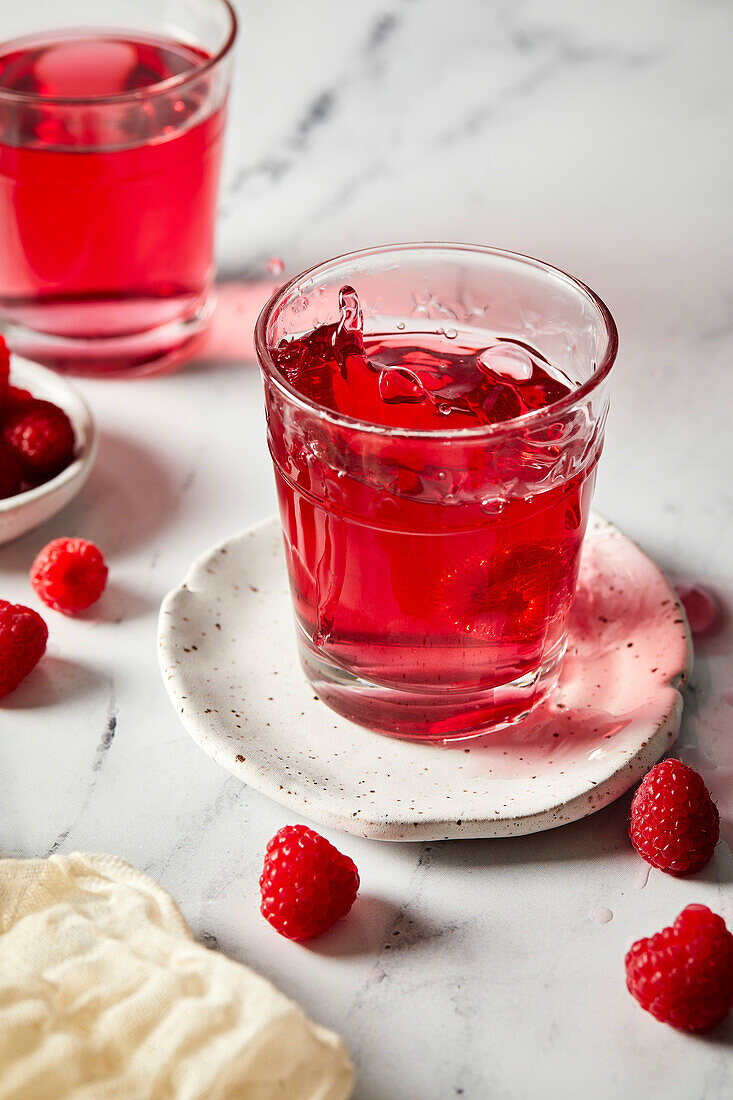 Splash photography of a glass of raspberry hibiscus ginger beer in a light marble background.