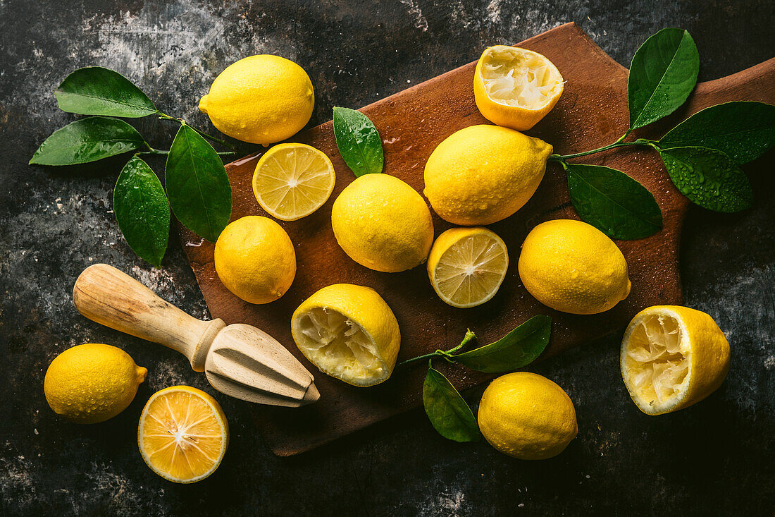 Freshly picked lemons with leaves, some halved, some juiced on antique cutting board with wooden juicer