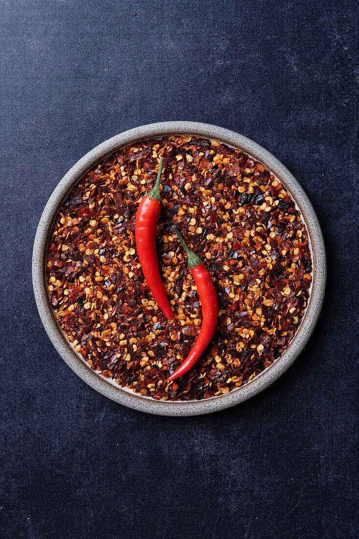 Chilli flakes on a plate of raw chillies on a blue background