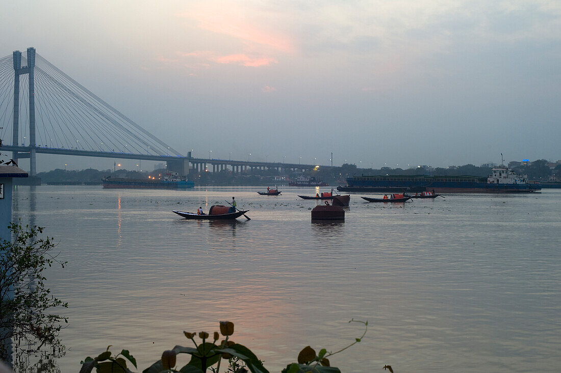 Gondeln rudern auf dem Hooghly-Fluss in Richtung der Vidyasagar Setu-Brücke bei Sonnenuntergang, Kolkata (Kalkutta), Westbengalen, Indien, Asien