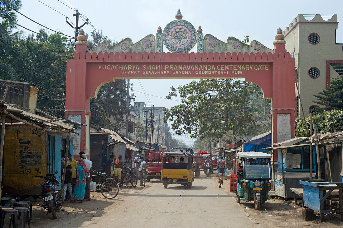 A commemorative archway to the backstreet market quarter with buyers and local traffic, Puri, the oldest of India's four holiest Hindu religious centres, Puri, State of Odisha, India, Asia