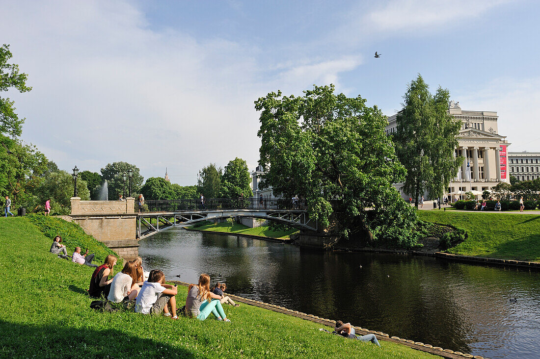 Young people on the bank of the Canal surrounding the Old Town of Riga, in front of the National Opera House, Riga, Latvia, Baltic region, Europe