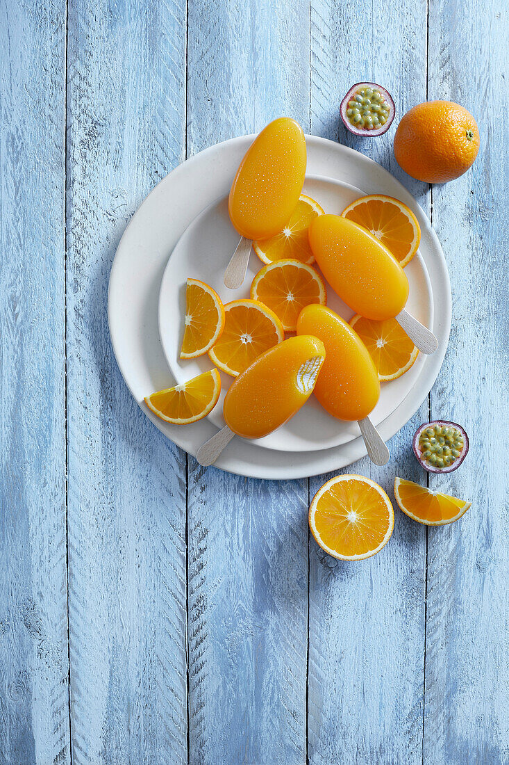 Orange passion fruit popsicles on freshly cut orange slices on a white plate, on a blue background