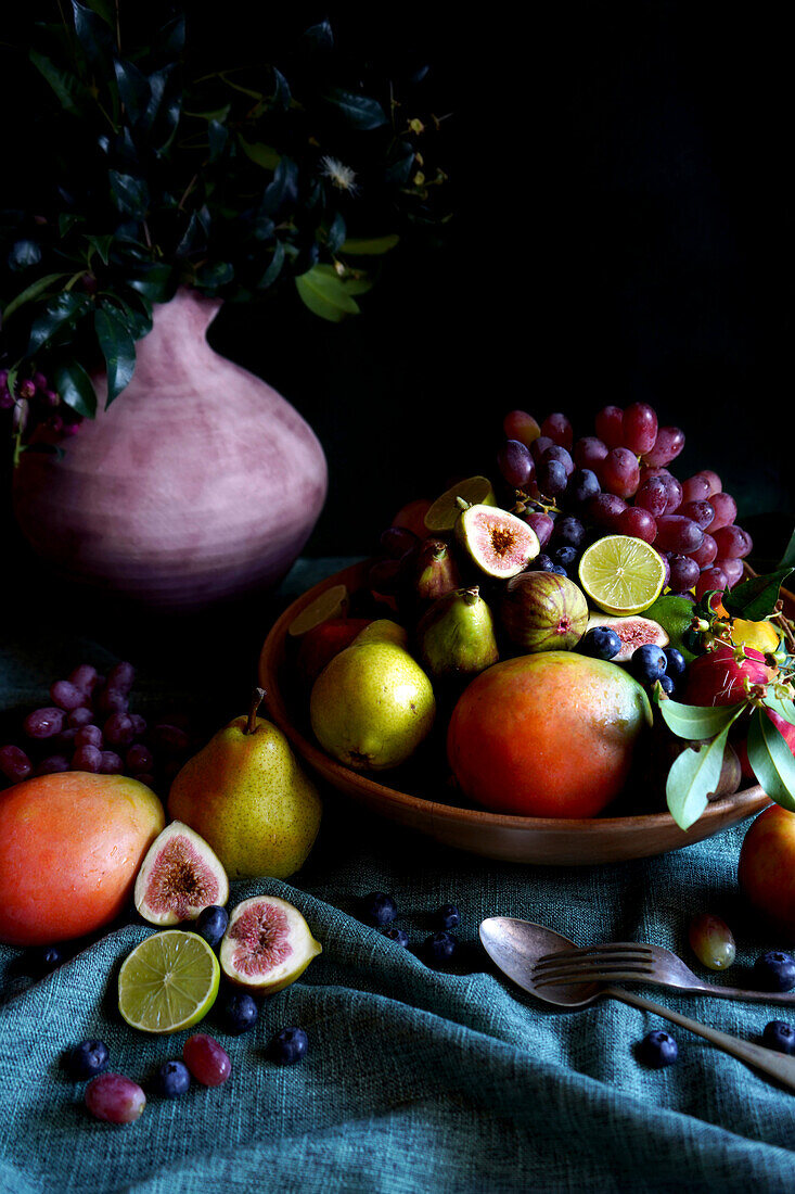 Saisonale Herbstfruchtschale mit Äpfeln, Birnen, Mangos, Feigen, Limetten und Weintrauben.