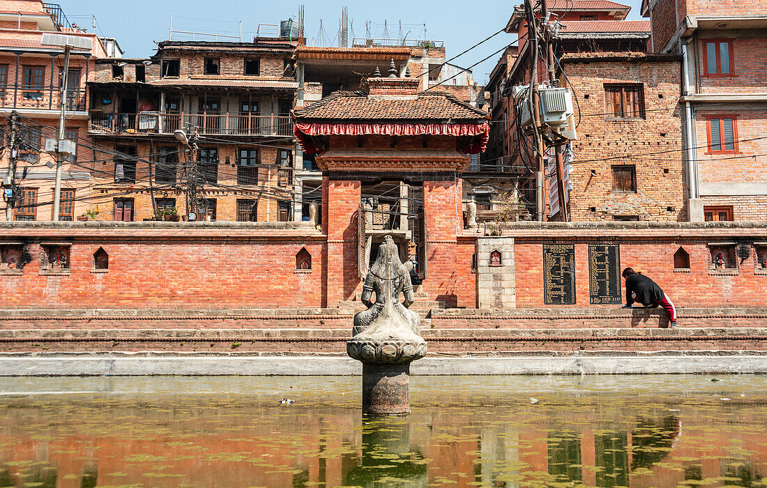 Shiva-Statue im grünen Wasser, Tekha Pukhu (Tekha Pokhari) Wasserbecken mit traditioneller Backsteinarchitektur von Bhaktapur, Nepal, Asien