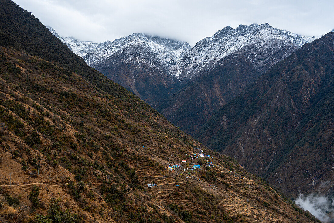 Blick entlang des weiten Tals mit hoch aufragenden Schneebergen und dem Dorf Sherpagaon an den Hängen, der Langtang-Tal-Trek, Himalaya, Nepal, Asien