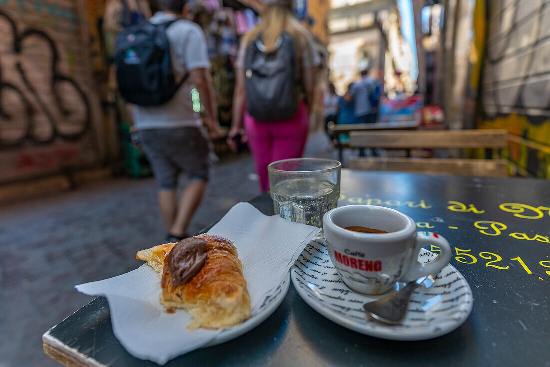 Blick auf ein Paar, das in der belebten Via San Biagio Dei Librai, Neapel, Kampanien, Italien, Europa, an einem Espresso-Kaffee auf einem Cafétisch vorbeigeht