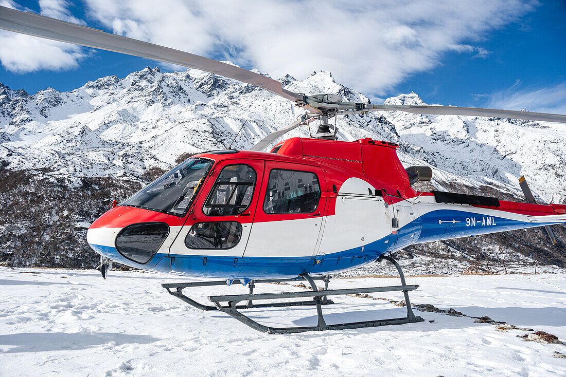 Nicht markierter Hubschrauber auf einem Schneefeld vor hoher verschneiter Berglandschaft, Langtang Valley Trek, Himalaya, Nepal, Asien