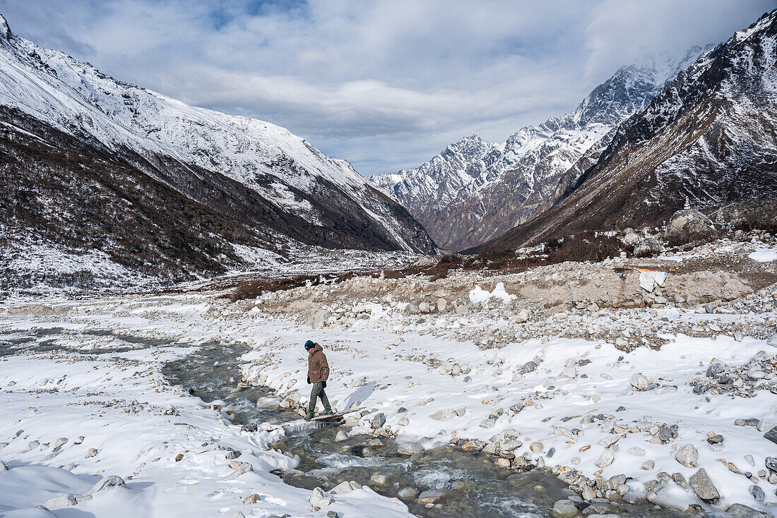 Männlicher Wanderer überquert einen gefrorenen Fluss in diesem verschneiten Hochtal, Langtang Valley Trek, Himalaya, Nepal, Asien