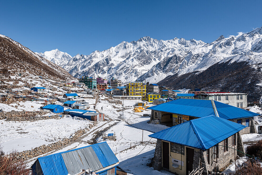 Blaue Dächer und farbenfrohe Hütten der Kyanjin Gompa mit Bergpanorama der umliegenden eisigen Gipfel, Langtang Valley Trek, Himalaya, Nepal, Asien