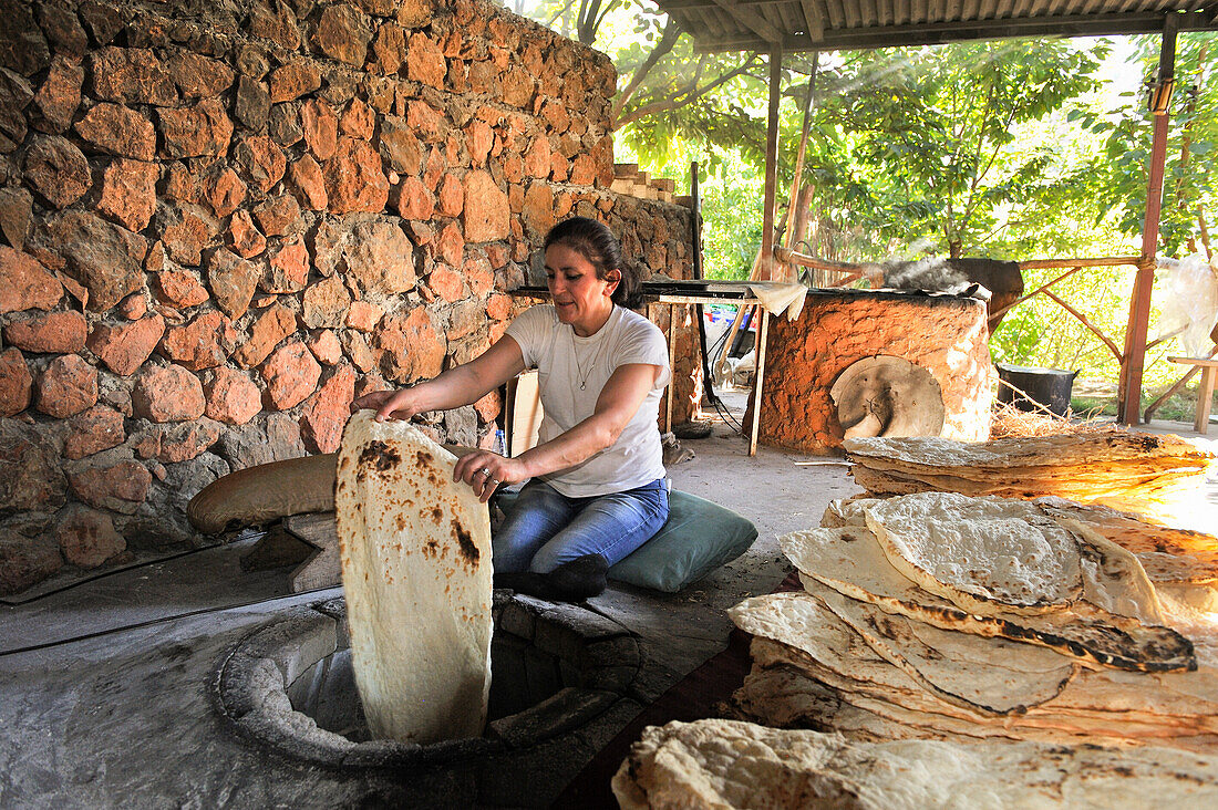 Frau bei der Zubereitung von Lavash (dünnes, ungesäuertes Fladenbrot) in einem Tandoor, auf Armenisch Tonir genannt, in einem Restaurant neben dem Noravank-Kloster, nahe Yeghegnadzor, Armenien, Eurasien