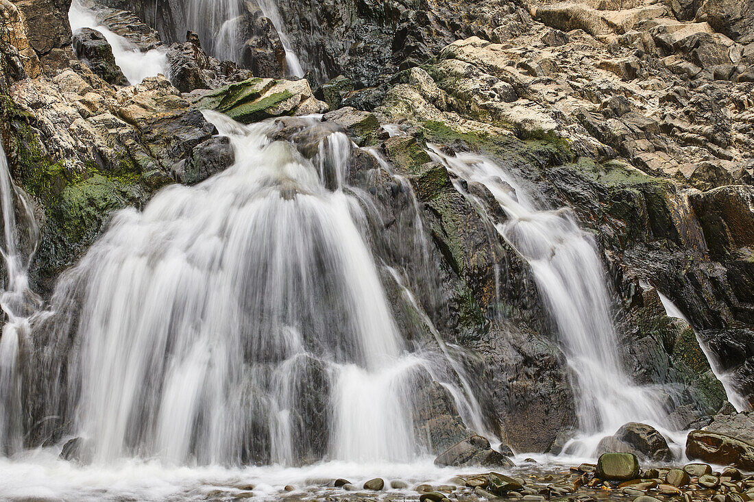 Wasserfall, der sich über eine felsige Klippe ergießt, mit unscharfer Bewegung, resultierend aus einer langen Verschlusszeit; am Welcombe Mouth, Hartland, Nord-Devon, England, Vereinigtes Königreich, Europa