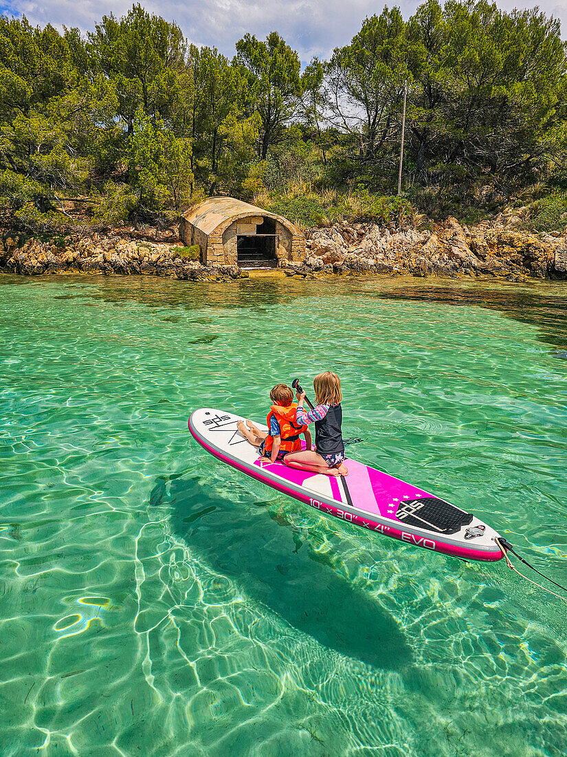 Kinder auf einem SUP in den türkisfarbenen Gewässern der Halbinsel Formentor, Mallorca, Balearen, Spanien, Mittelmeer, Europa