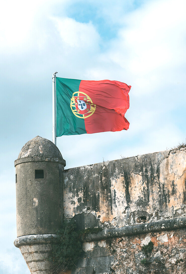 Ein verwittertes Steinkastell und eine portugiesische Flagge, die von einem Fahnenmast auf einem kleinen Turm weht, Lissabon, Portugal, Europa