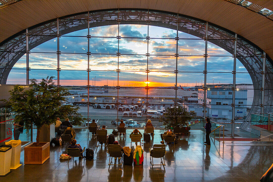 Passagiere betrachten den Sonnenuntergang in der Abflughalle des Flughafens Charles de Gaulle, Terminal 2F, Paris, Frankreich, Europa