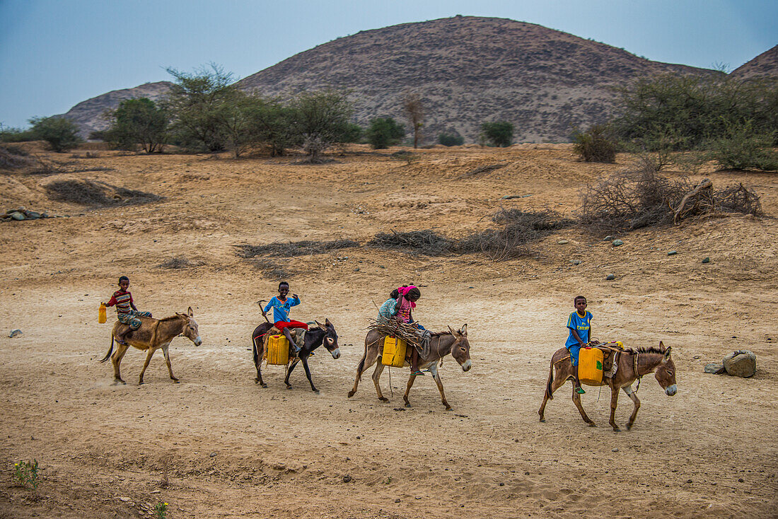 Junge Kinder reiten auf Eseln zu einem Wasserloch im Tiefland von Eritrea, Afrika